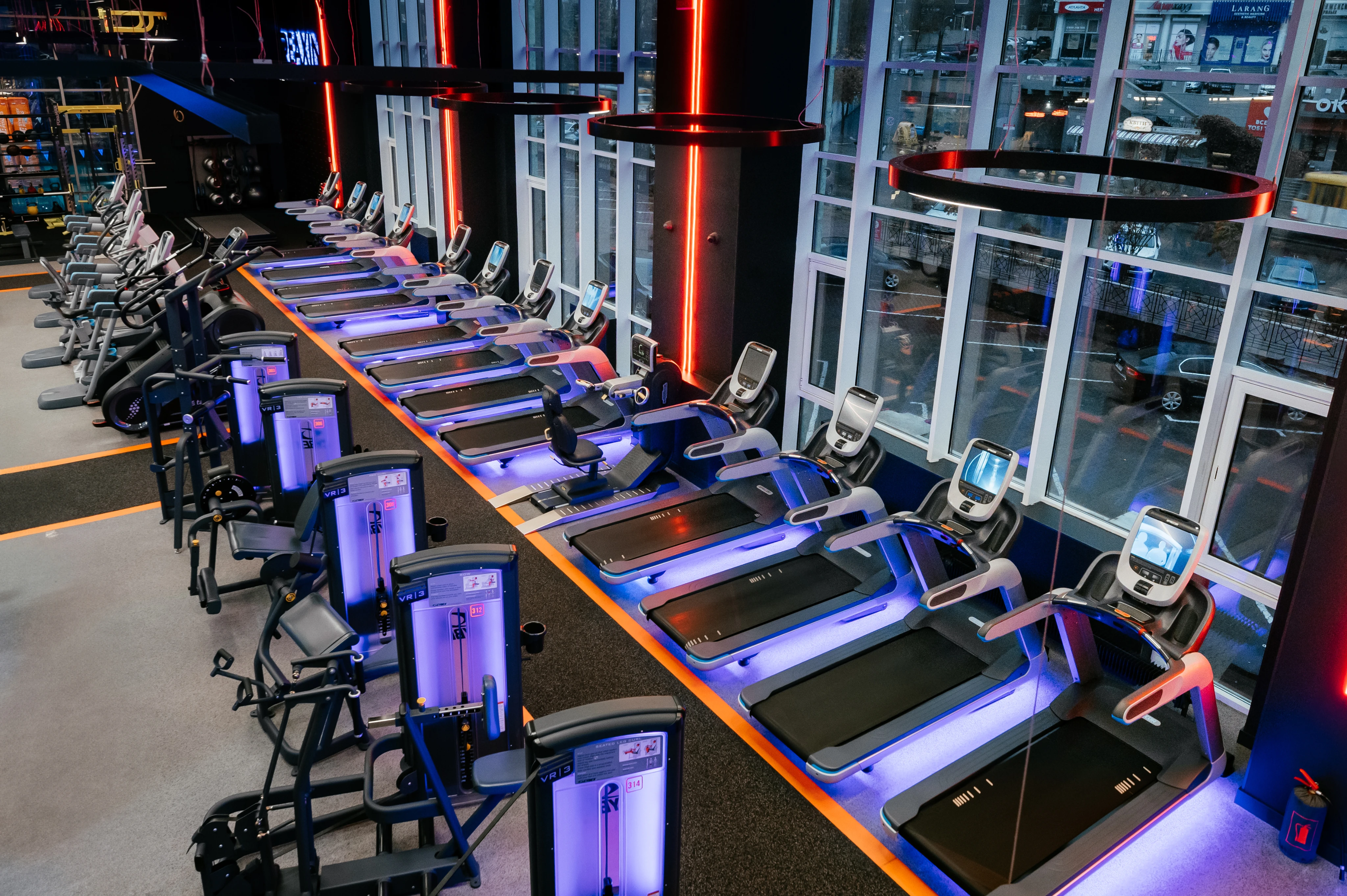 Беговые дорожки с неоновым освещением, современное оборудование и большие окна в помещении